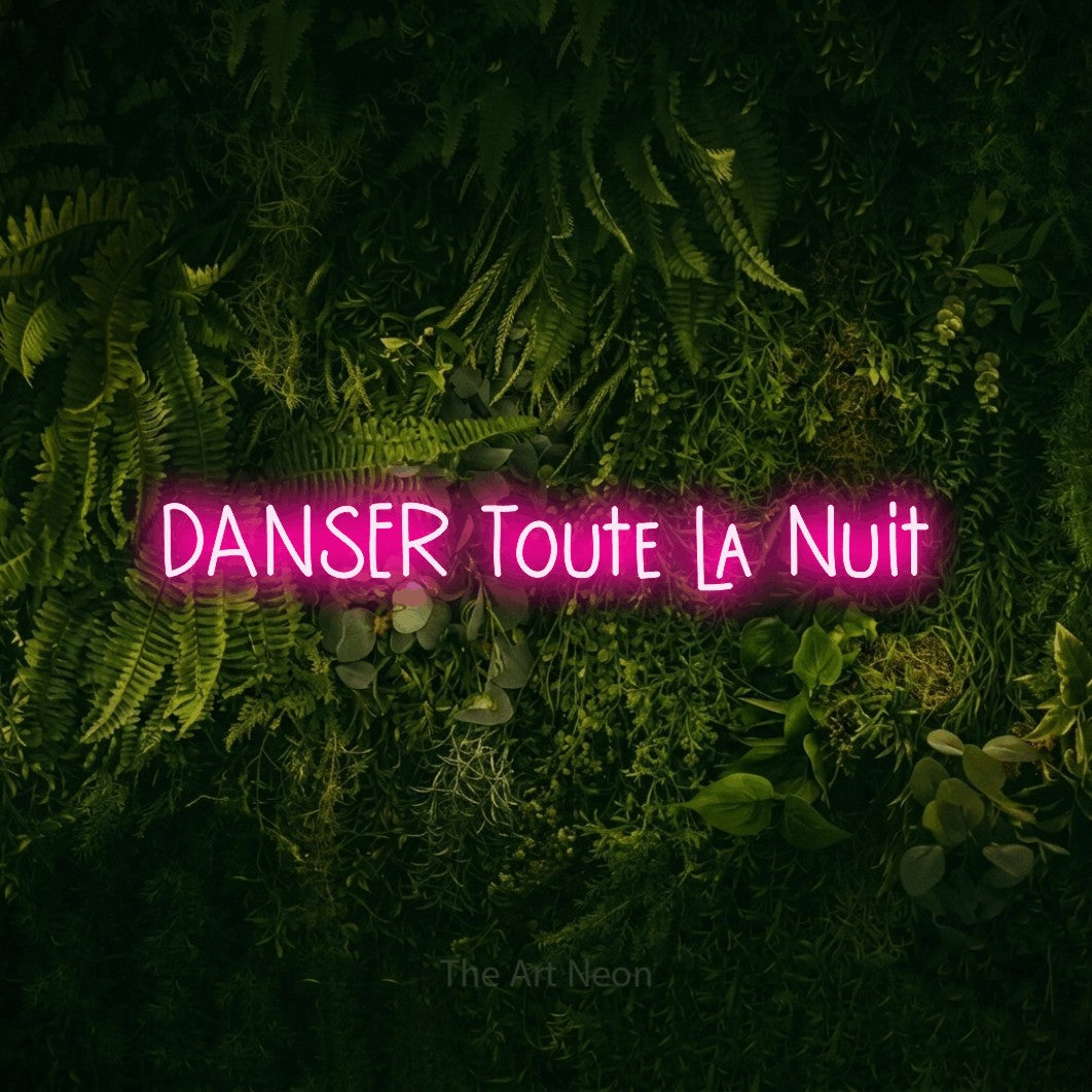 “Danser toute la nuit” LED neon sign in hot pink, with narrow hand-drawn lettering, shown against a dark moss and forest backdrop.
