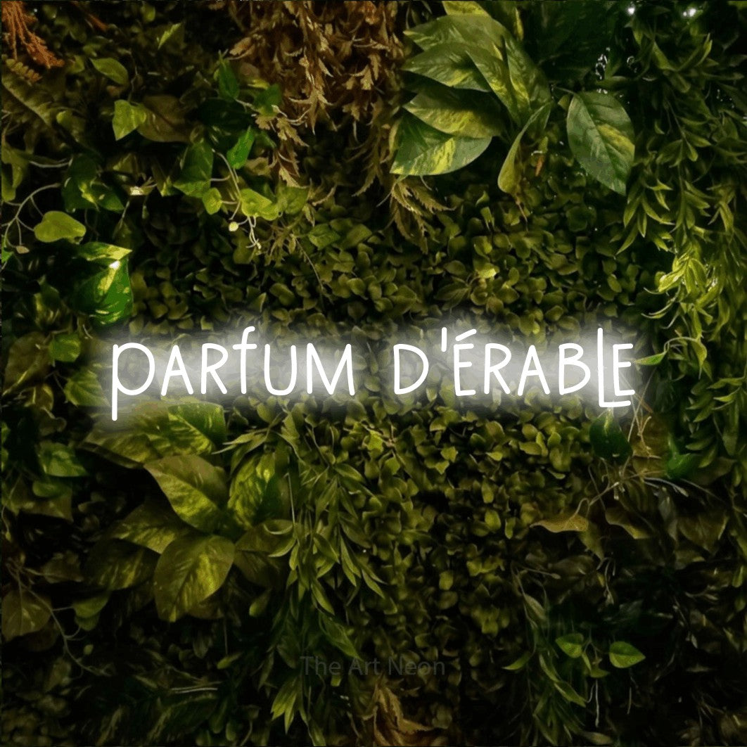 “Parfum d'érable” LED neon sign in cool white, with narrow hand-drawn lettering, shown against bright green and yellow foliage.