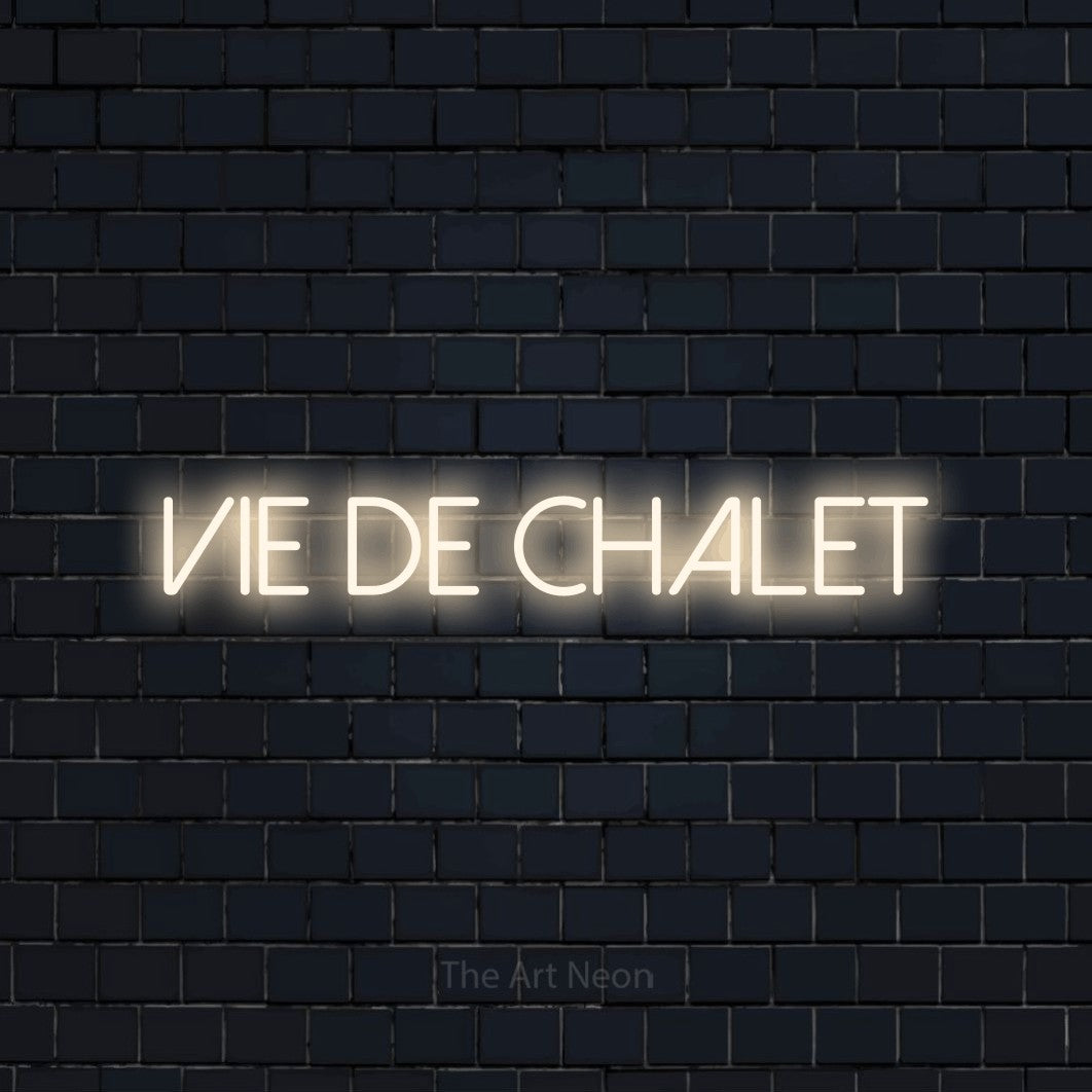 “Vie de chalet” LED neon sign in warm white, with thin sans-serif lettering, shown against a dark navy brick wall.