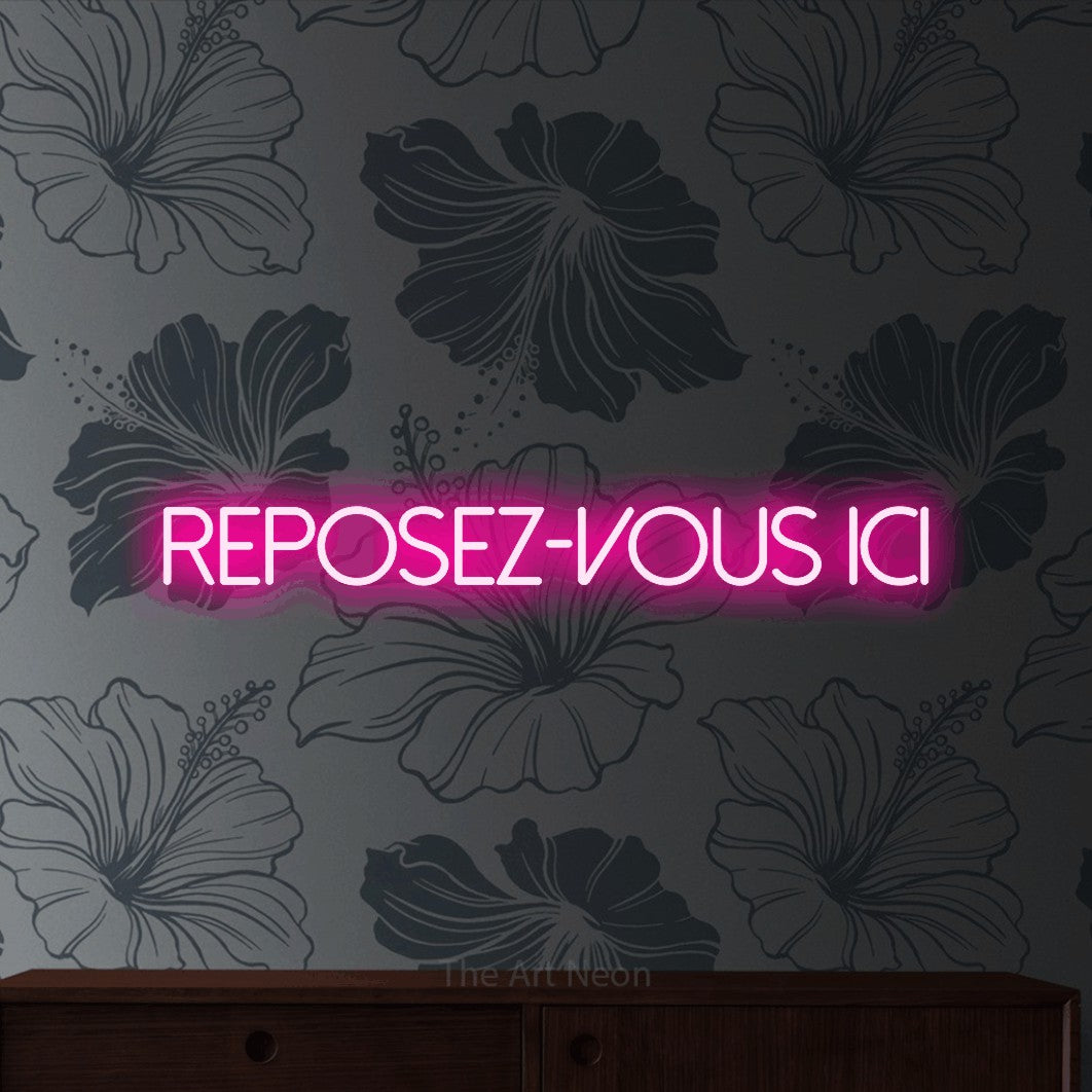 “Reposez-vous ici” LED neon sign in hot pink, with thin sans-serif lettering, shown against a grey floral-patterned wall.