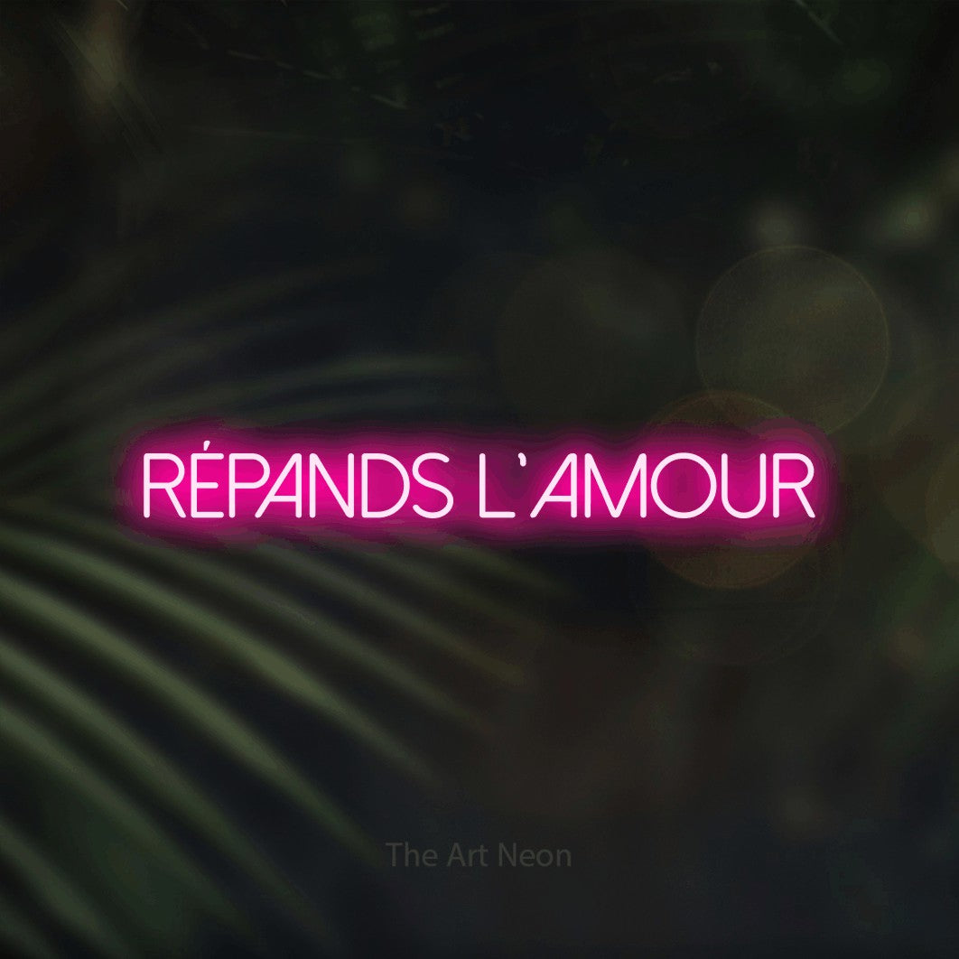 “Répands l'amour” LED neon sign in hot pink, with thin sans-serif lettering, shown against a blurred palm and bokeh-light backdrop.