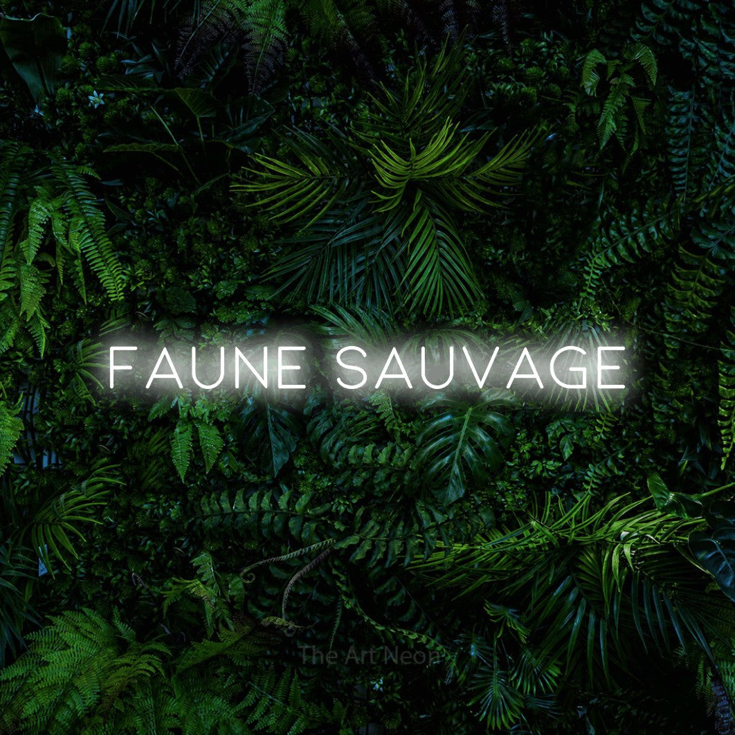 Composition en néon LED « Faune sauvage » en blanc froid, en lettres fines et espacées, mise en valeur devant un feuillage tropical dense, pour un décor inspiré de la nature.