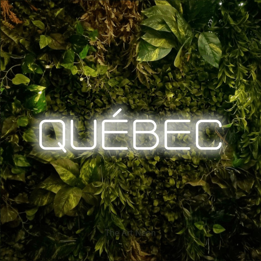 “Québec” LED neon sign in cool white, with rounded geometric lettering, shown against bright green and yellow foliage.