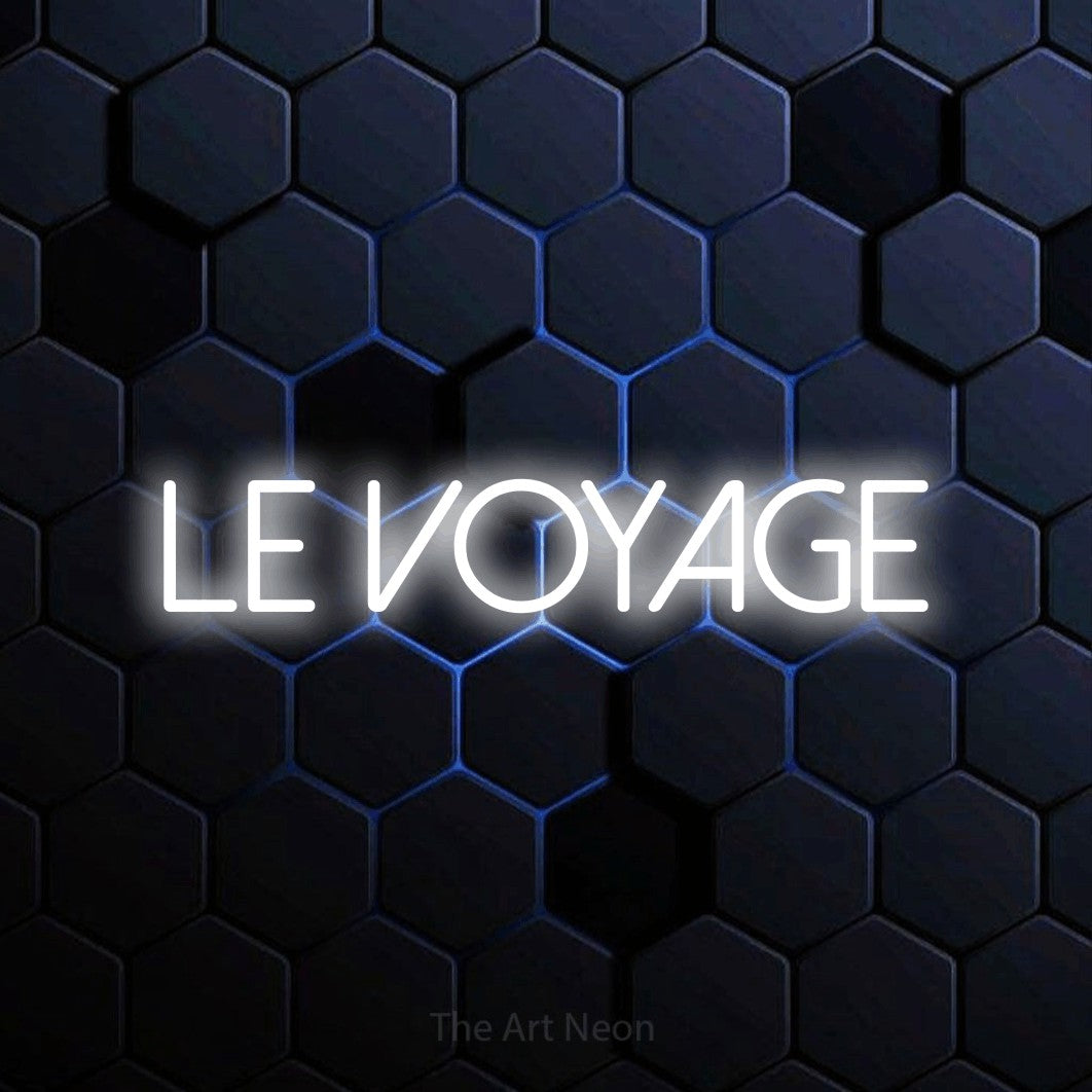 “Le voyage” LED neon sign in cool white, with thin sans-serif lettering, shown against a dark blue honeycomb pattern.