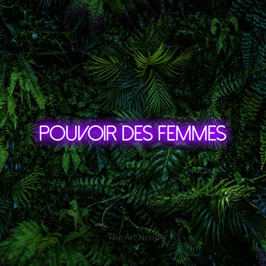 “Pouvoir des femmes” LED neon sign in purple, with thin sans-serif lettering, shown against dense tropical foliage.