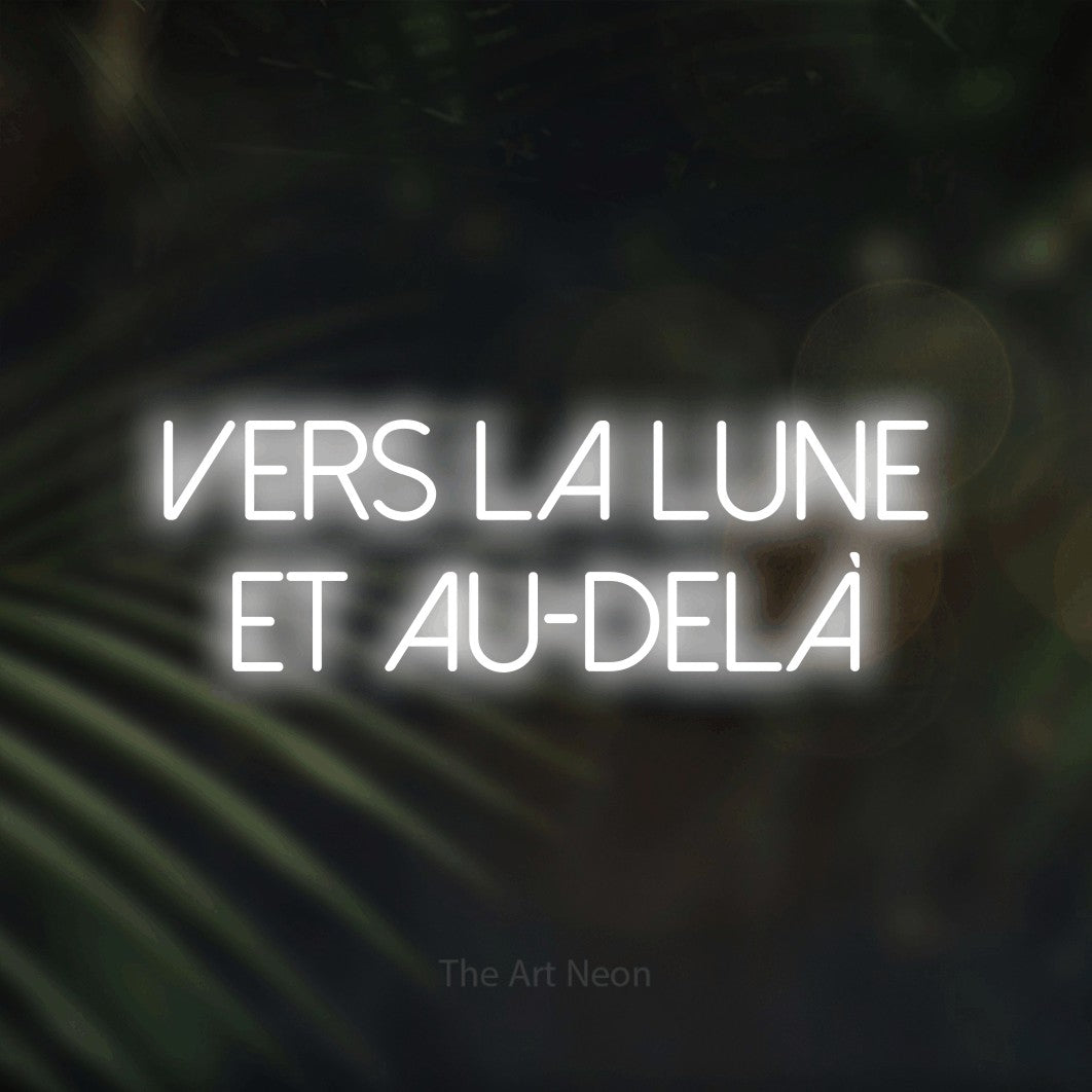 “Vers la lune et au-delà” LED neon sign in cool white, with thin sans-serif lettering across 2 lines, shown against a blurred palm and bokeh-light backdrop.