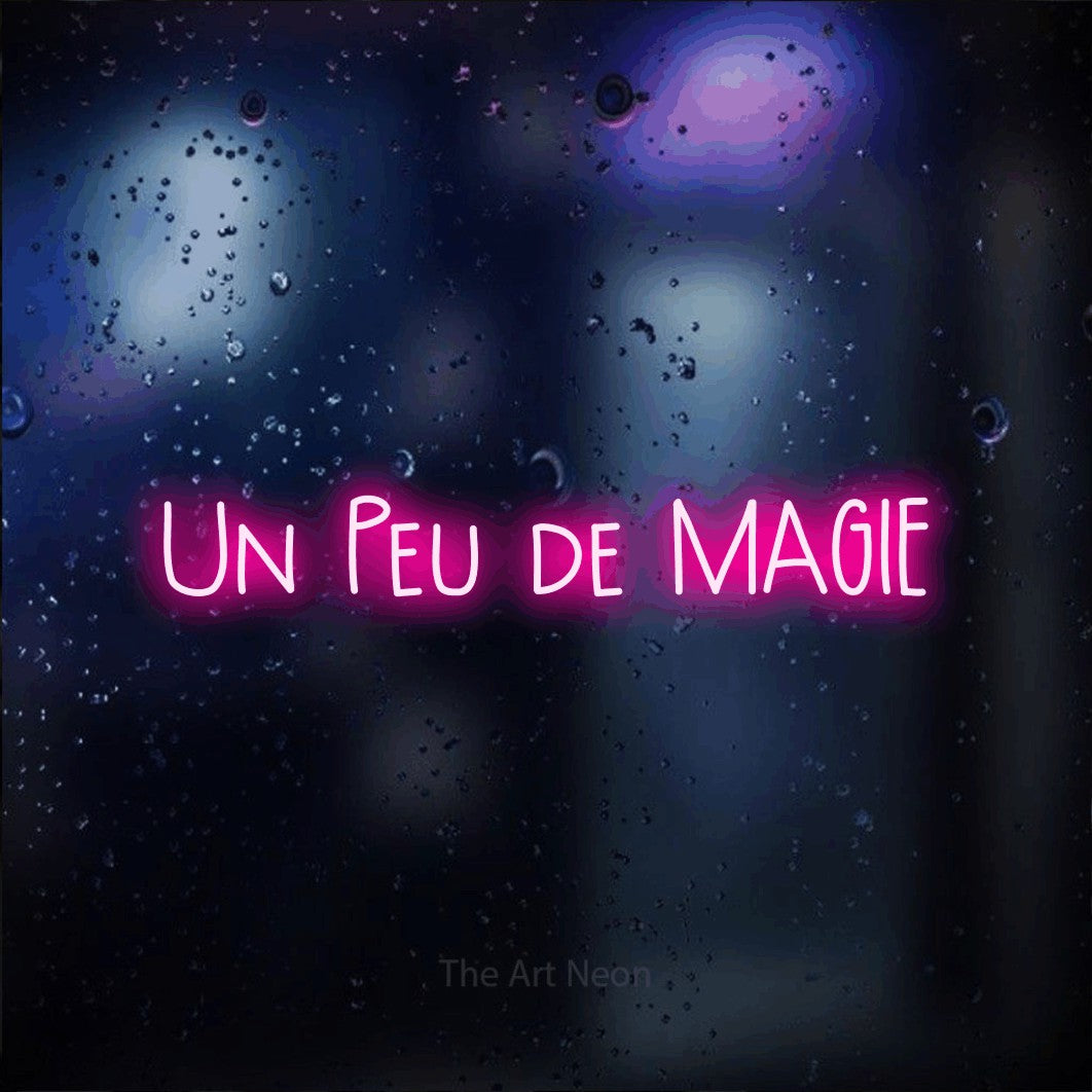 “Un peu de magie” LED neon sign in hot pink, with narrow hand-drawn lettering, shown against glass with blue and purple reflections.