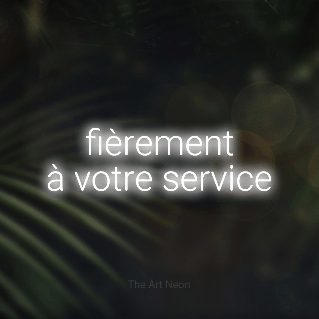 “Fièrement à votre service” LED neon sign in cool white, with rounded sans-serif lettering across 2 lines, shown against a blurred palm and bokeh-light backdrop.