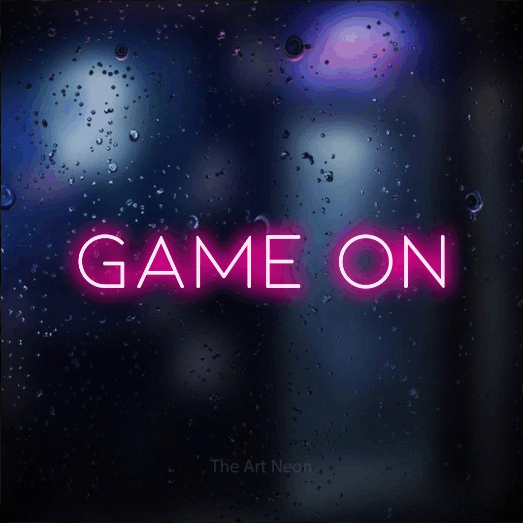 “Game on” LED neon sign in hot pink, with thin, widely spaced lettering, shown against glass with blue and purple reflections.