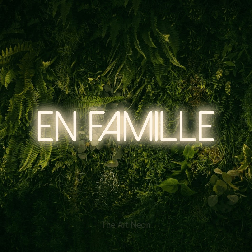 “En famille” LED neon sign in warm white, with thin sans-serif lettering, shown against a dark moss and forest backdrop.