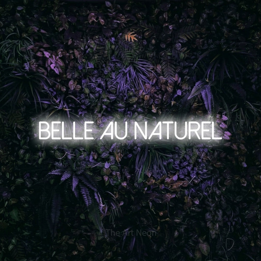 Lettrage en néon LED « Belle au naturel » en blanc froid, en lettres fines sans empattement, présenté sur un mur sombre aux fleurs violettes, pour un salon de beauté.