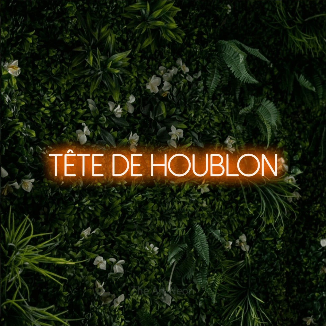 “Tête de houblon” LED neon sign in orange, with thin sans-serif lettering, shown against a dense green plant wall.