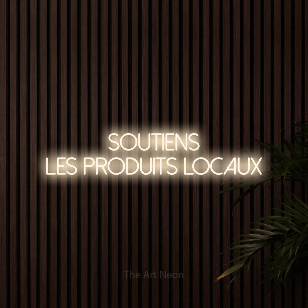 “Soutiens les produits locaux” LED neon sign in warm white, with thin sans-serif lettering across 2 lines, shown against dark wooden wall slats.