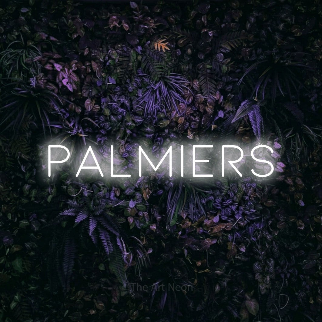 Décoration murale en néon LED « Palmiers » en blanc froid, en lettres fines et espacées, installée sur un mur sombre aux fleurs violettes, pour un décor inspiré de la nature.