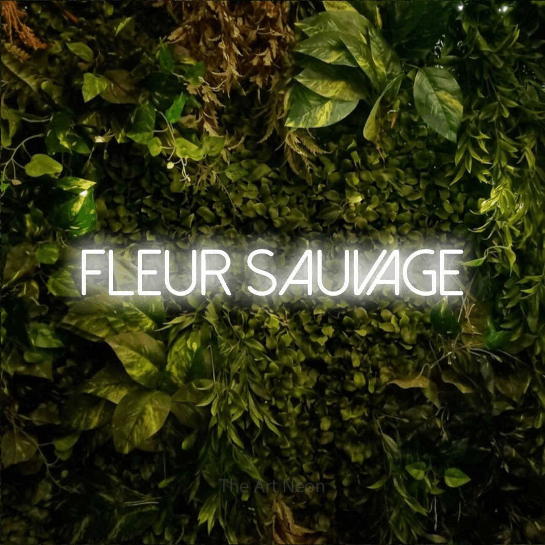 “Fleur sauvage” LED neon sign in cool white, with thin sans-serif lettering, shown against bright green and yellow foliage.