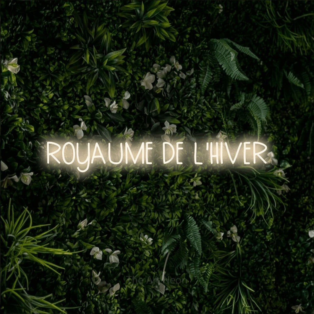 Composition en néon LED « Royaume de l'hiver » en blanc chaud, en lettres étroites dessinées à la main, mise en valeur sur un mur végétal vert et dense, pour un décor canadien.