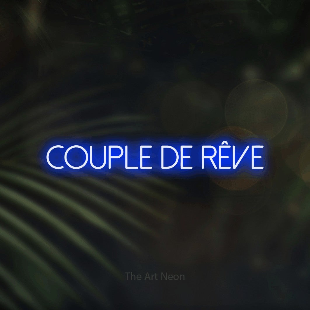 “Couple de rêve” LED neon sign in blue, with thin sans-serif lettering, shown against a blurred palm and bokeh-light backdrop.