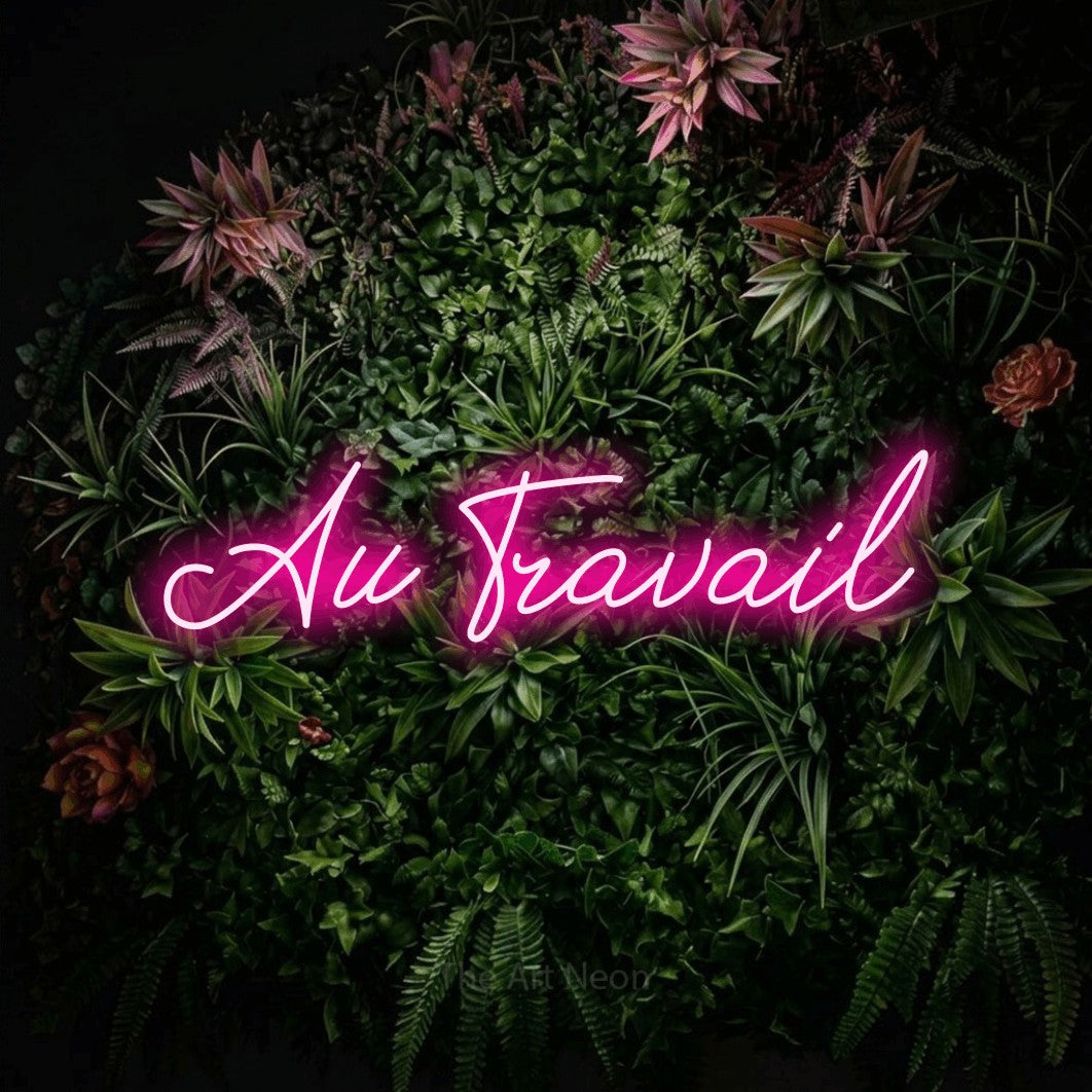 “Au travail” LED neon sign in hot pink, with cursive lettering, shown against a flowering plant wall.