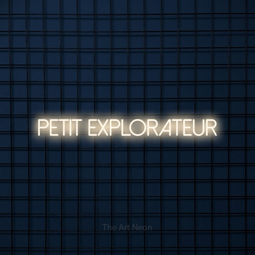 “Petit explorateur” LED neon sign in warm white, with thin sans-serif lettering, shown against a dark blue grid.