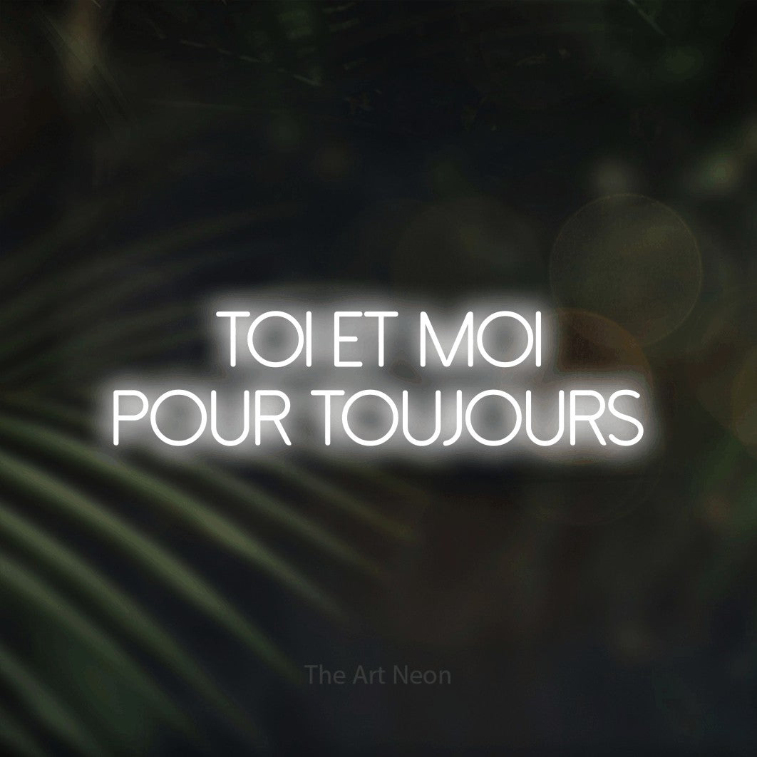 “Toi et moi pour toujours” LED neon sign in cool white, with thin sans-serif lettering across 2 lines, shown against a blurred palm and bokeh-light backdrop.