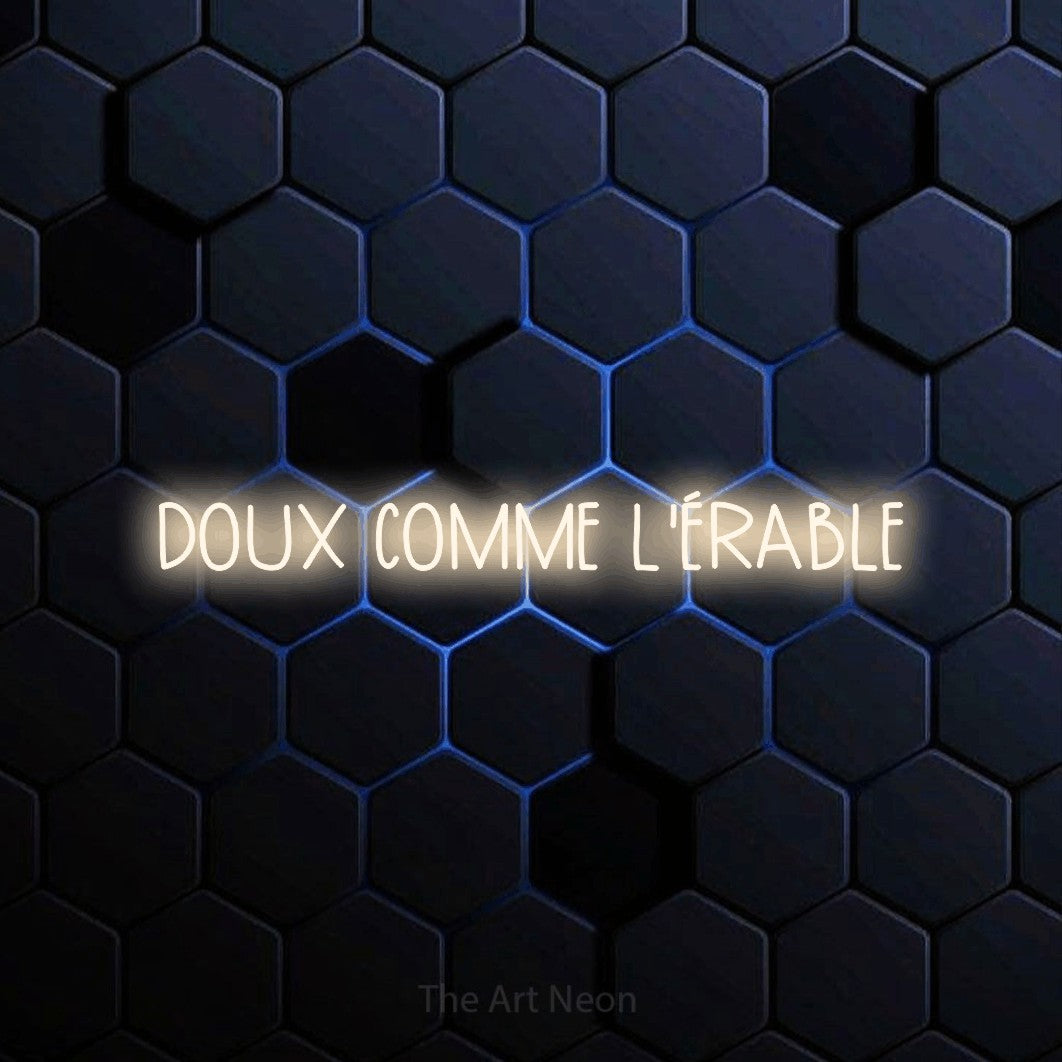 “Doux comme l'érable” LED neon sign in warm white, with narrow hand-drawn lettering, shown against a dark blue honeycomb pattern.