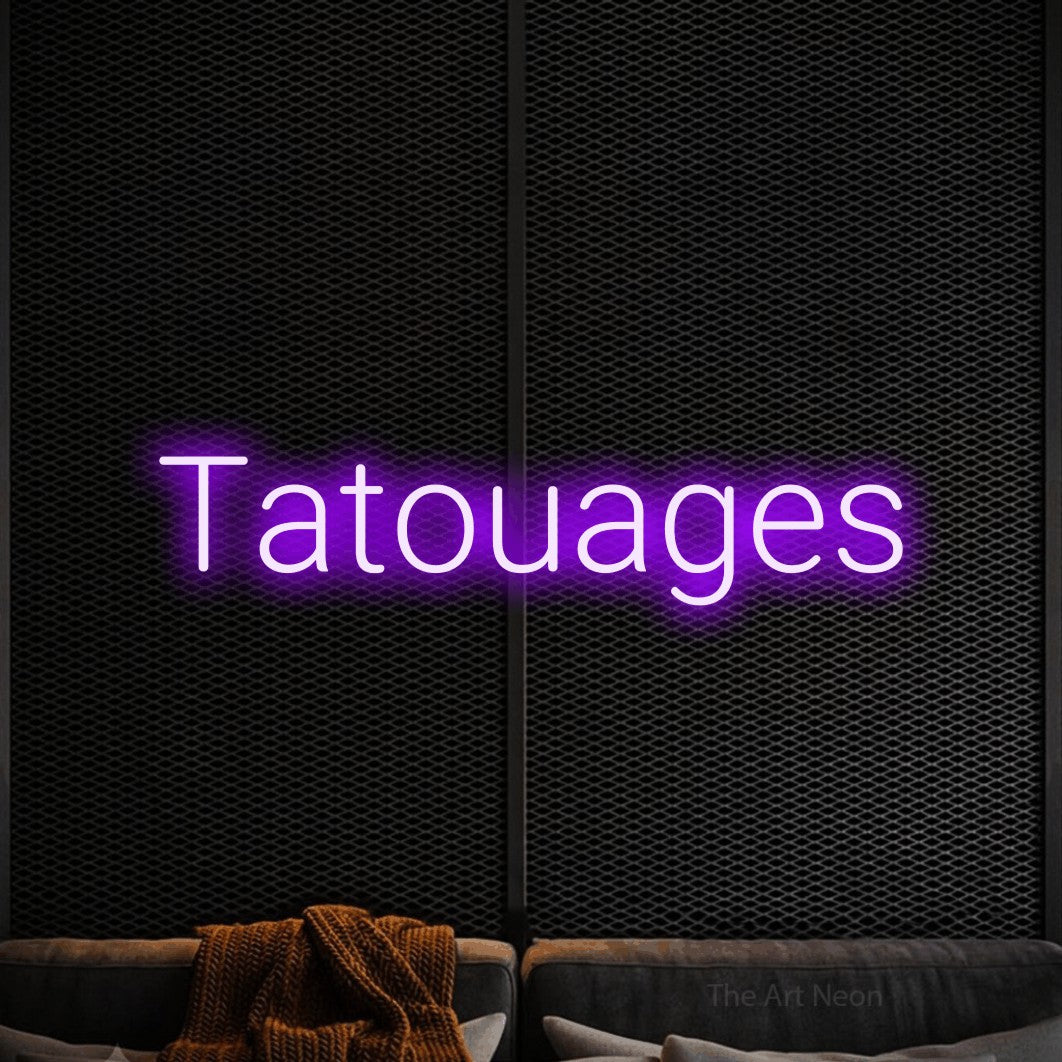“Tatouages” LED neon sign in purple, with rounded sans-serif lettering, shown against a modern dark-toned seating area.