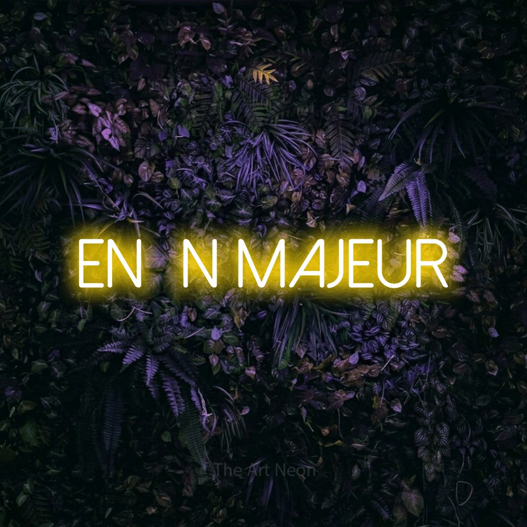 Lettrage en néon LED « Enfin majeur » en jaune, en lettres fines sans empattement, présenté sur un mur sombre aux fleurs violettes, pour une fête.