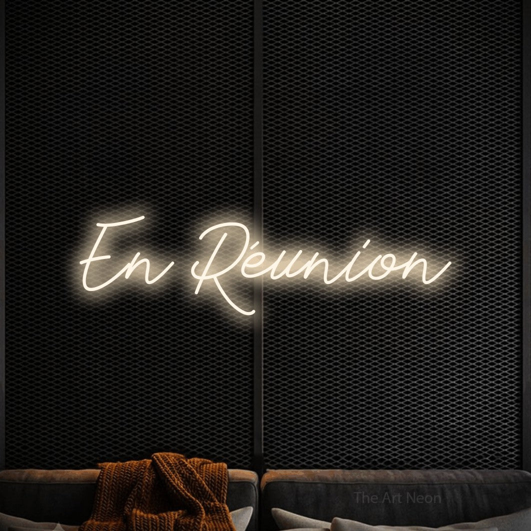 “En réunion” LED neon sign in warm white, with cursive lettering, shown against a modern dark-toned seating area.