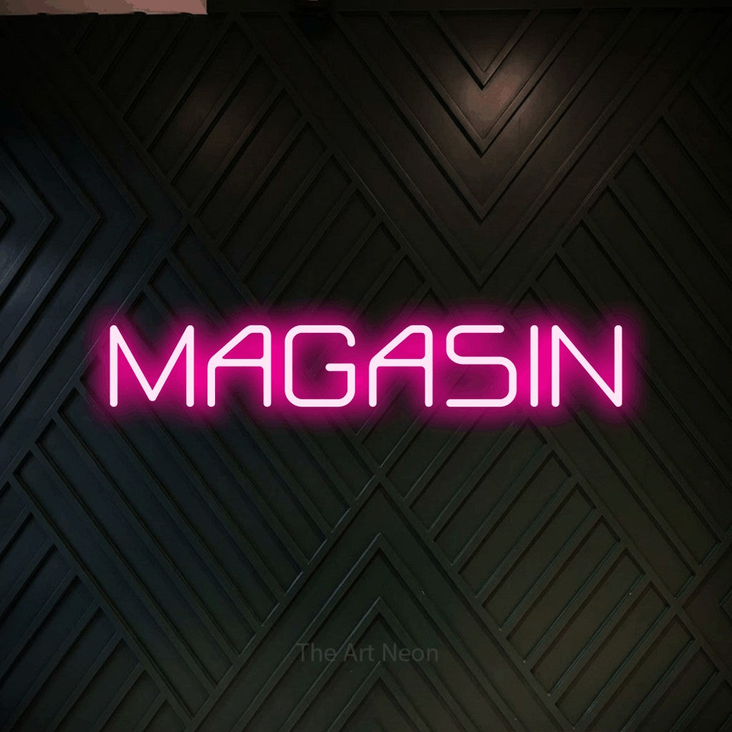 “Magasin” LED neon sign in hot pink, with rounded geometric lettering, shown against a black chevron-patterned wood wall.