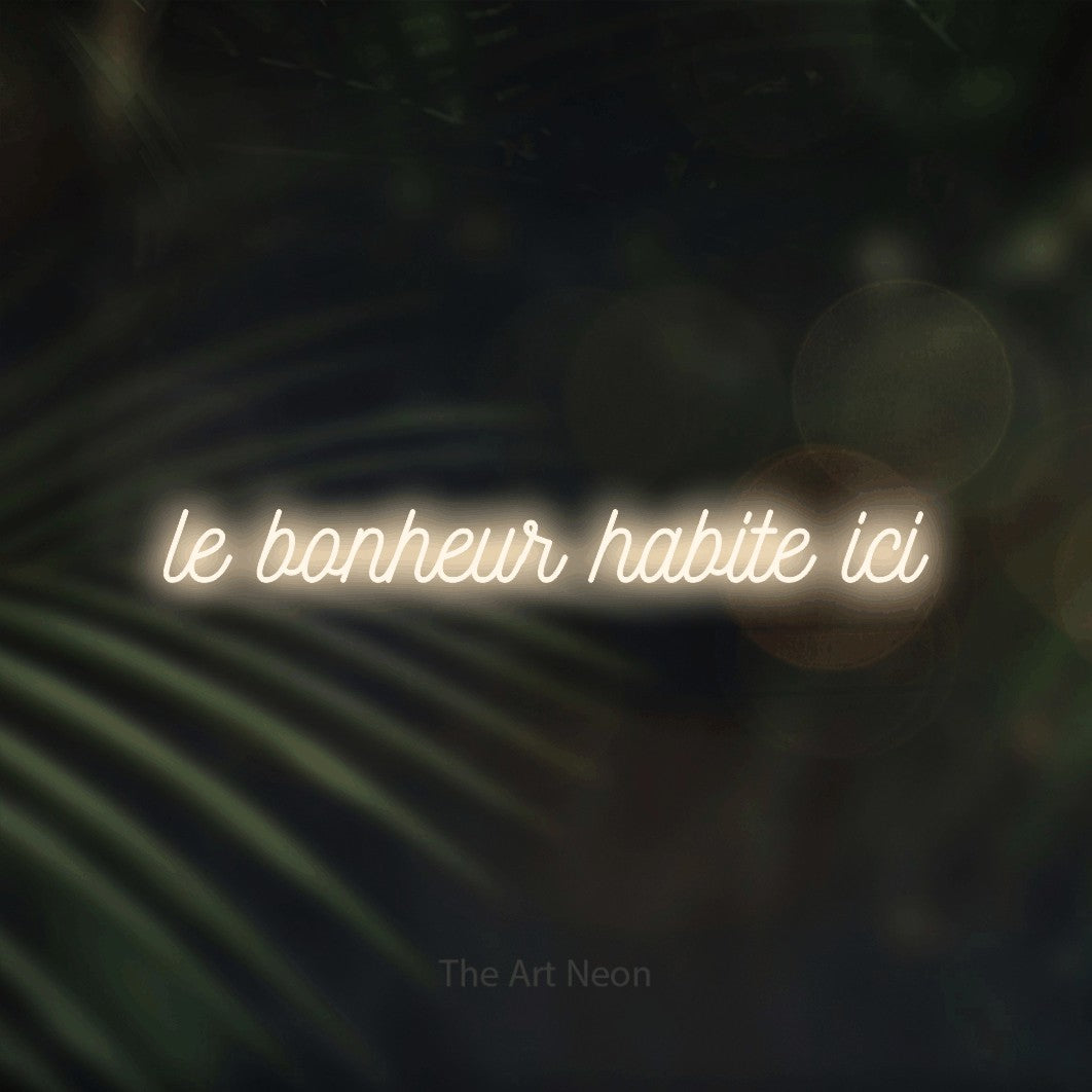 “Le bonheur habite ici” LED neon sign in warm white, with ornate cursive lettering, shown against a blurred palm and bokeh-light backdrop.
