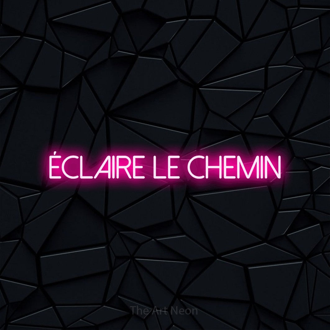 “Éclaire le chemin” LED neon sign in hot pink, with thin sans-serif lettering, shown against a black polygonal surface.