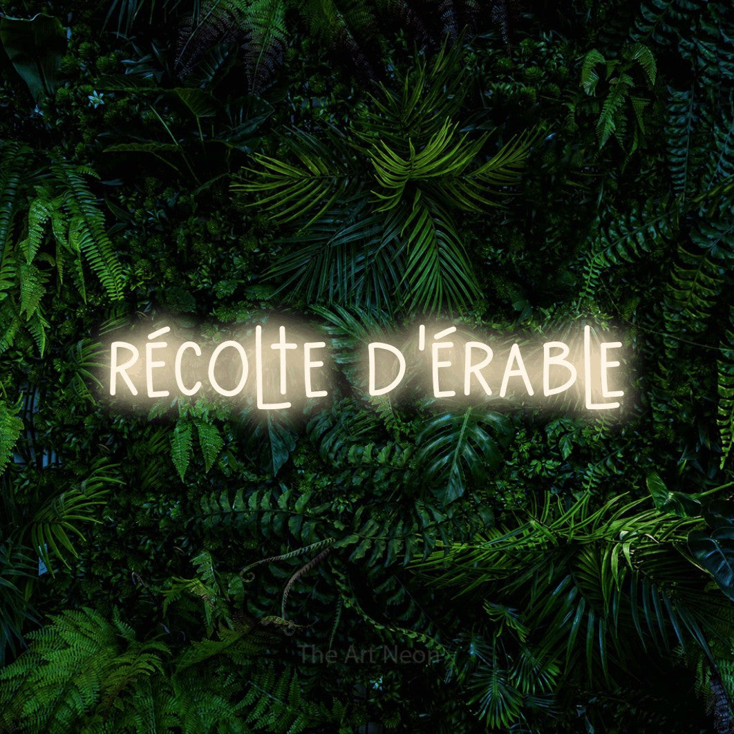 “Récolte d'érable” LED neon sign in warm white, with narrow hand-drawn lettering, shown against dense tropical foliage.