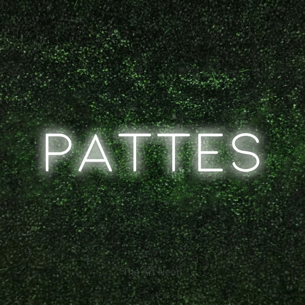 “Pattes” LED neon sign in cool white, with thin, widely spaced lettering, shown against a textured green hedge.