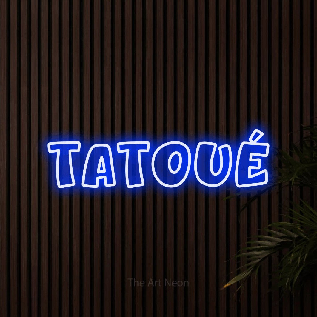“Tatoué” LED neon sign in blue, with rounded outline lettering, shown against dark wooden wall slats.