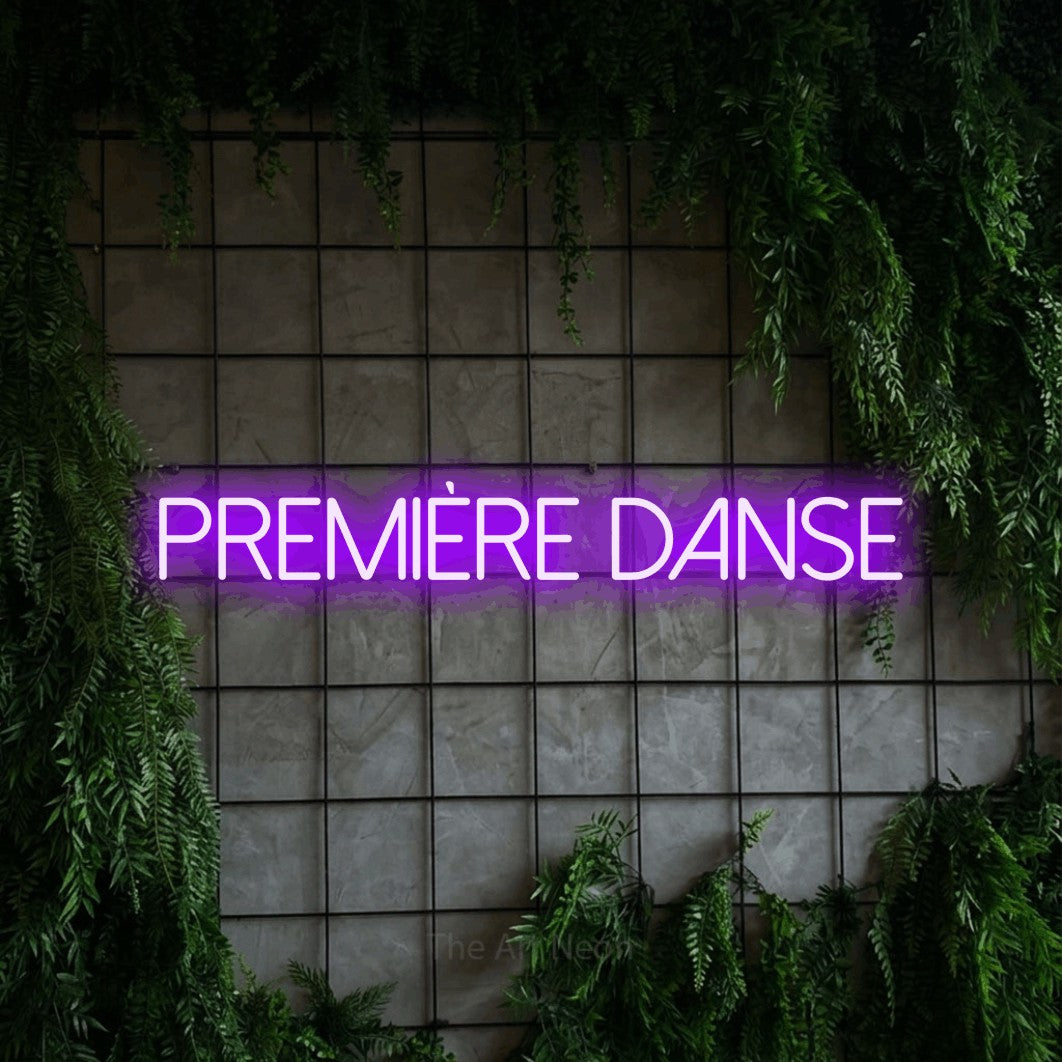 Décoration murale en néon LED « Première danse » en violet, en lettres fines sans empattement, installée sur une grille de béton couverte de lierre, pour une réception de mariage.