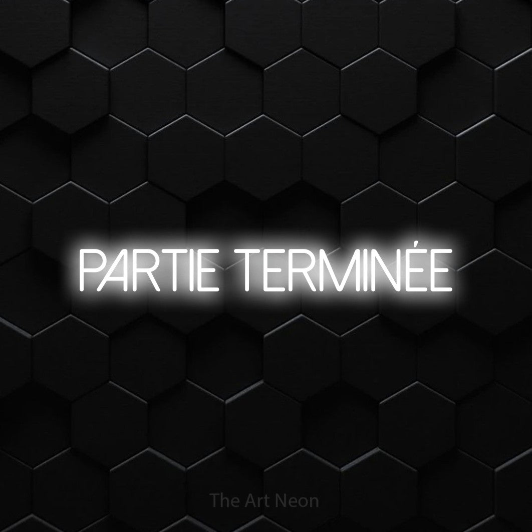 Lettrage en néon LED « Partie terminée » en blanc froid, en lettres fines sans empattement, présenté sur un mur de carreaux hexagonaux noirs, pour un espace de jeux vidéo.