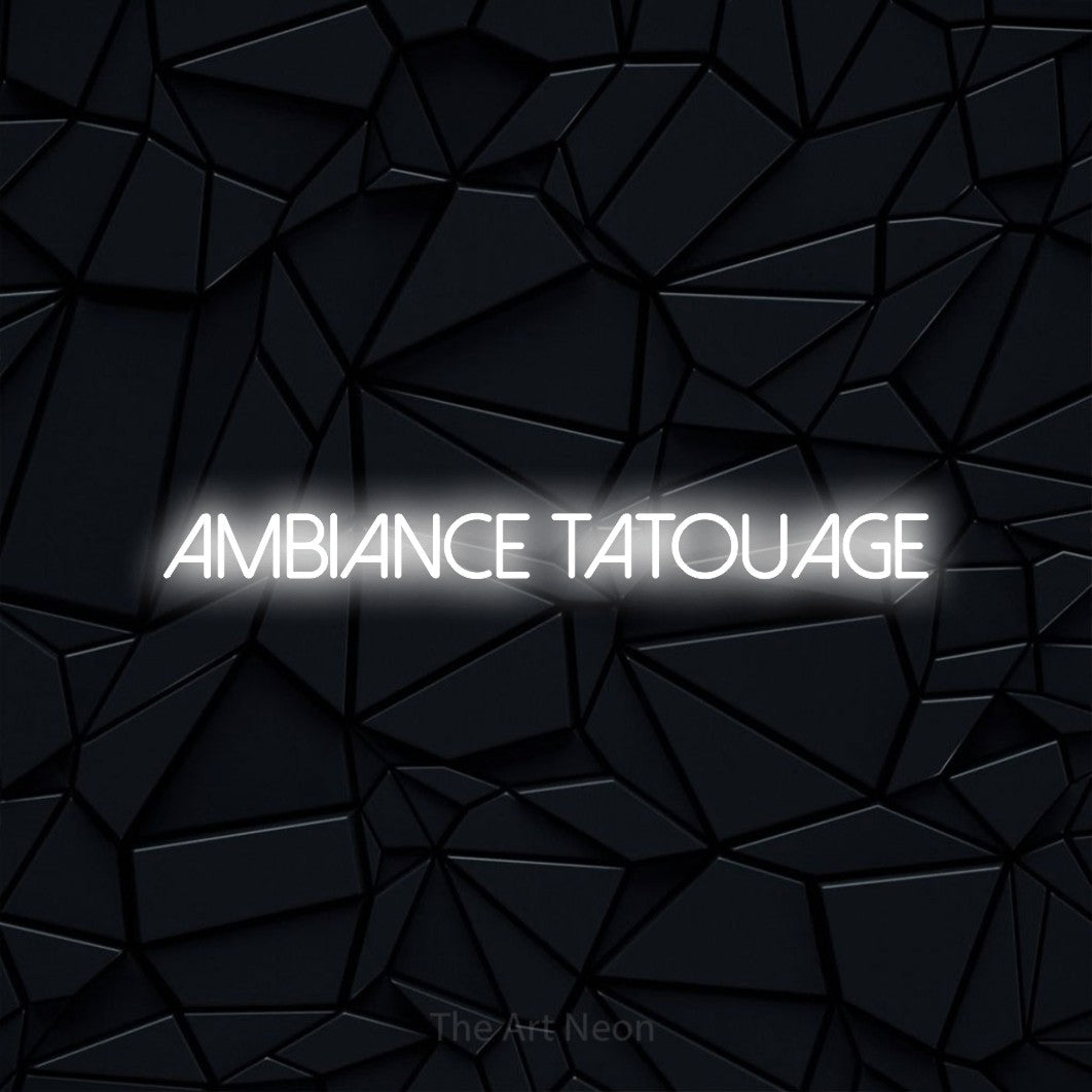 “Ambiance tatouage” LED neon sign in cool white, with thin sans-serif lettering, shown against a black polygonal surface.