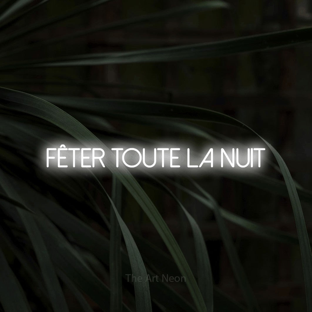 “Fêter toute la nuit” LED neon sign in cool white, with thin sans-serif lettering, shown against a close-up of dark foliage.