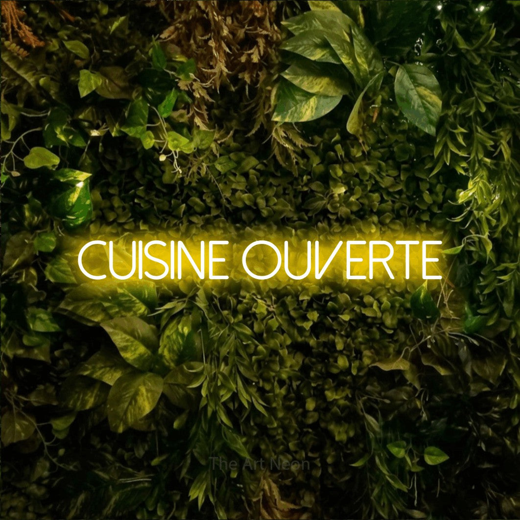 “Cuisine ouverte” LED neon sign in yellow, with thin sans-serif lettering, shown against bright green and yellow foliage.