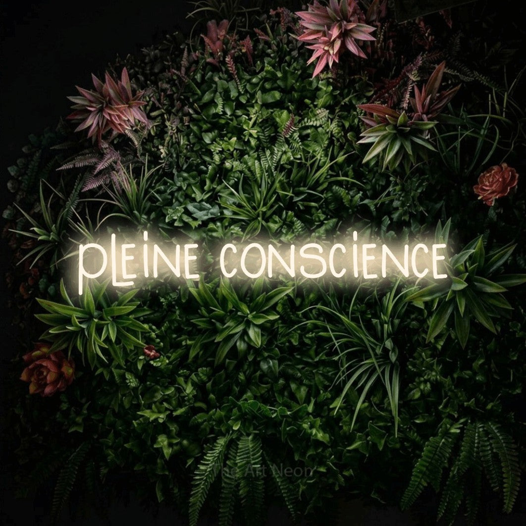 “Pleine conscience” LED neon sign in warm white, with narrow hand-drawn lettering, shown against a flowering plant wall.