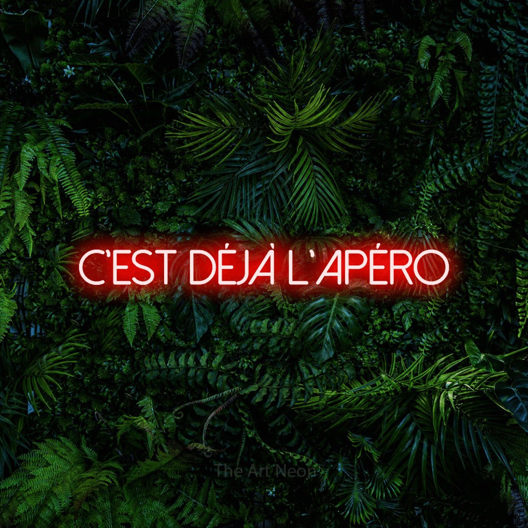 Néon LED « C'est déjà l'apéro » en rouge, en lettres fines sans empattement, mis en scène devant un feuillage tropical dense, pour un bar à la maison.