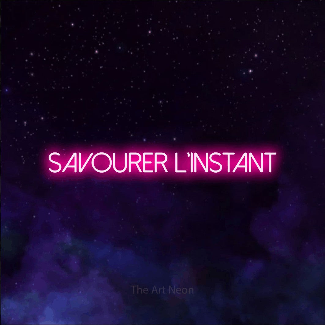 “Savourer l'instant” LED neon sign in hot pink, with thin sans-serif lettering, shown against a purple galaxy backdrop.