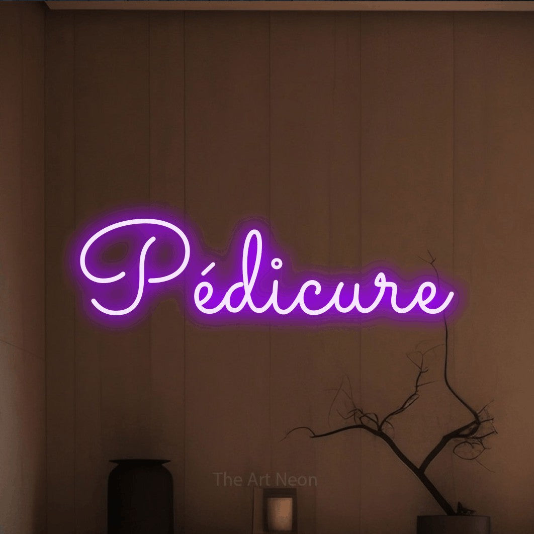 Décoration murale en néon LED « Pédicure » en violet, en lettres cursives aux boucles marquées, installée dans un intérieur épuré aux tons terre, pour un salon de beauté.