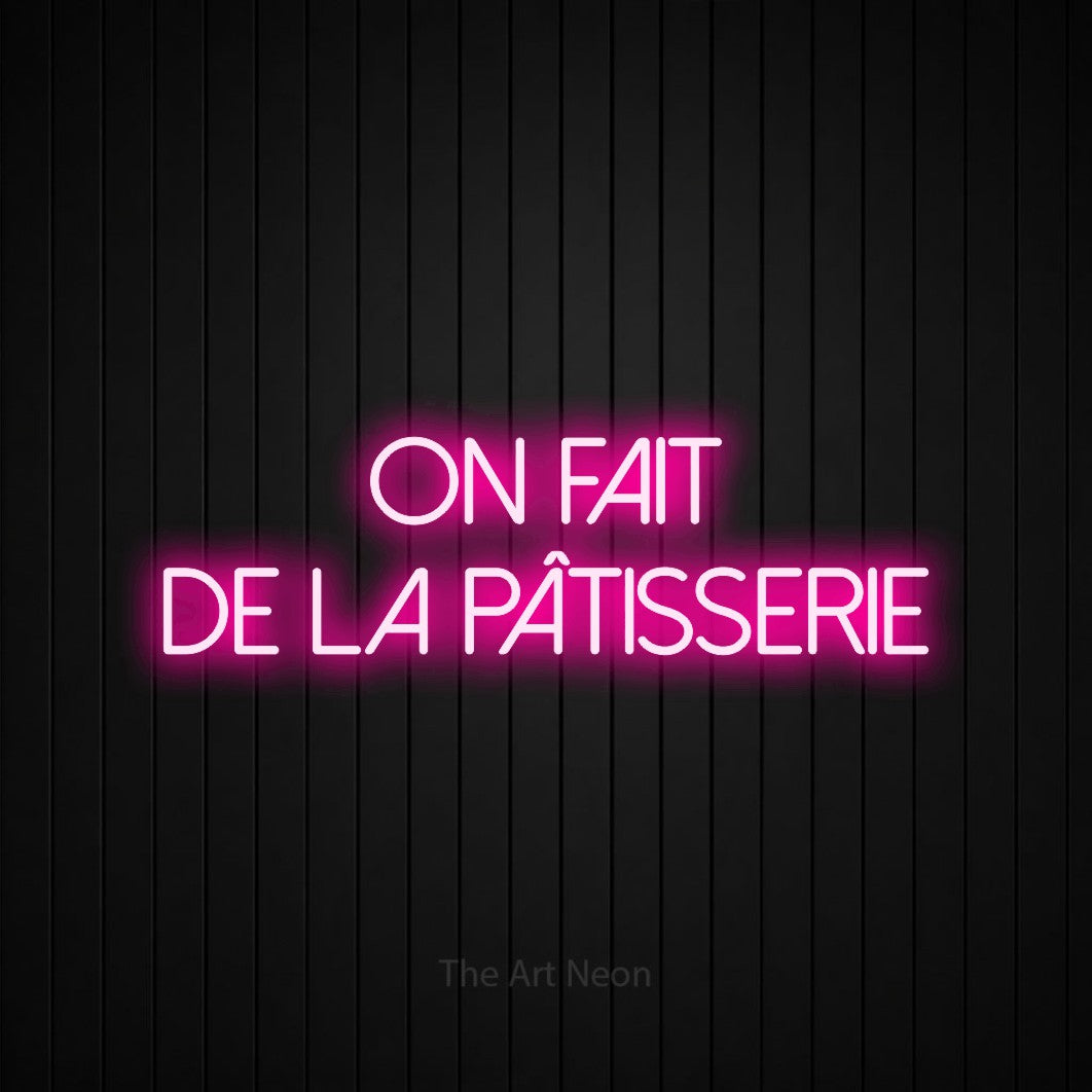“On fait de la pâtisserie” LED neon sign in hot pink, with thin sans-serif lettering across 2 lines, shown against black vertical wall slats.