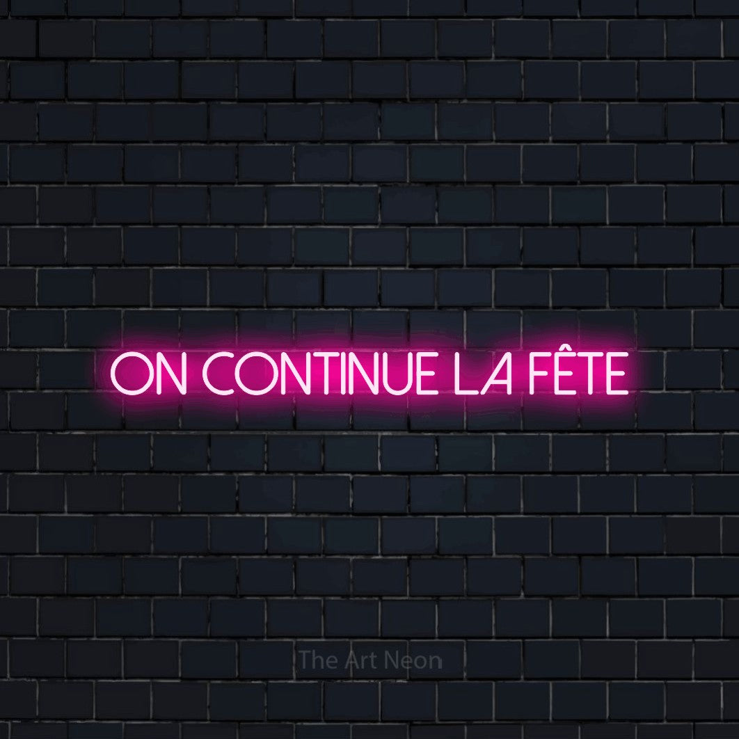 Enseigne néon LED « On continue la fête » en rose vif, en lettres fines sans empattement, présentée sur un mur de briques bleu marine foncé, pour une fête.