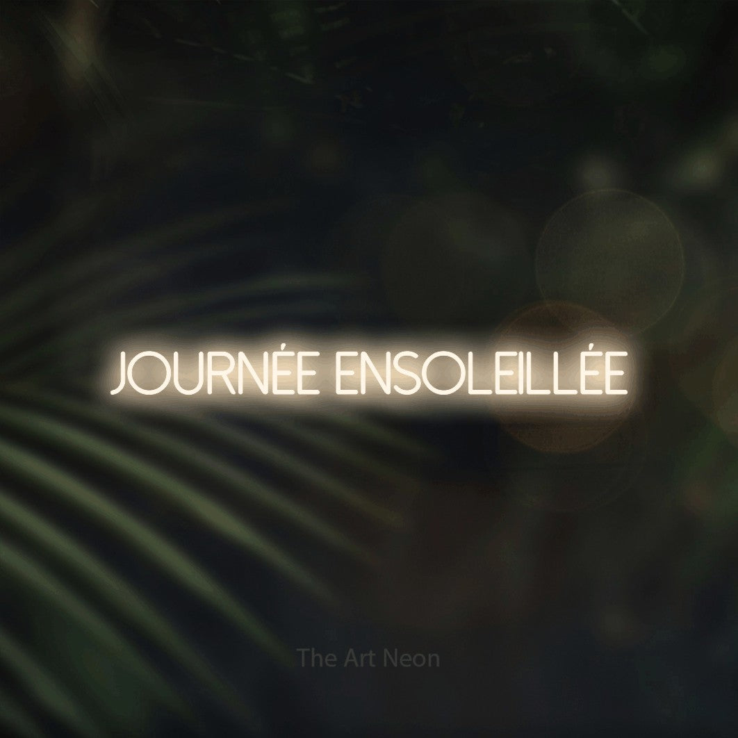 “Journée ensoleillée” LED neon sign in warm white, with thin sans-serif lettering, shown against a blurred palm and bokeh-light backdrop.