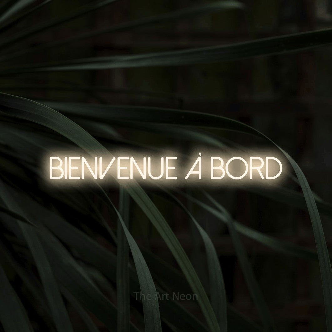 “Bienvenue à bord” LED neon sign in warm white, with thin sans-serif lettering, shown against a close-up of dark foliage.