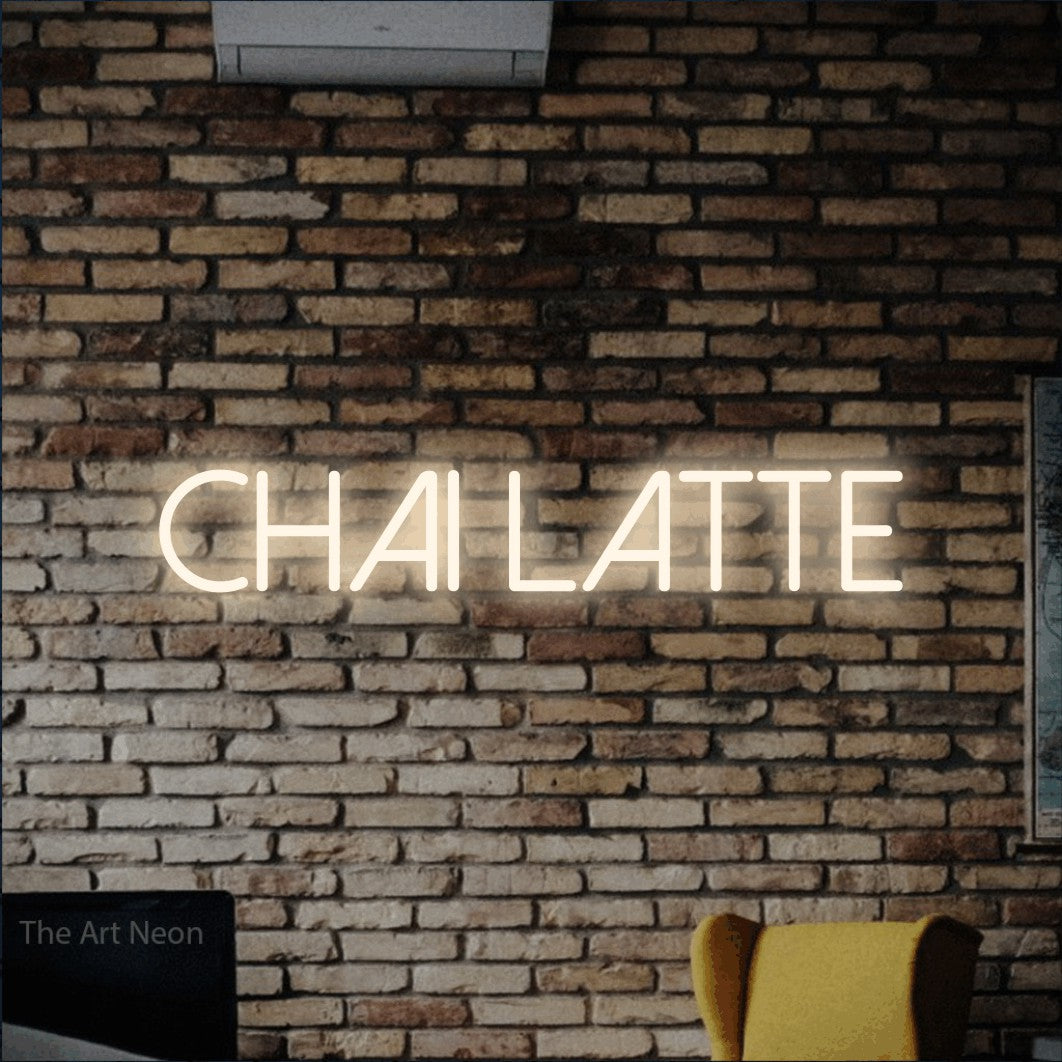 “Chai latte” LED neon sign in warm white, with thin sans-serif lettering, shown against warm-toned brickwork.