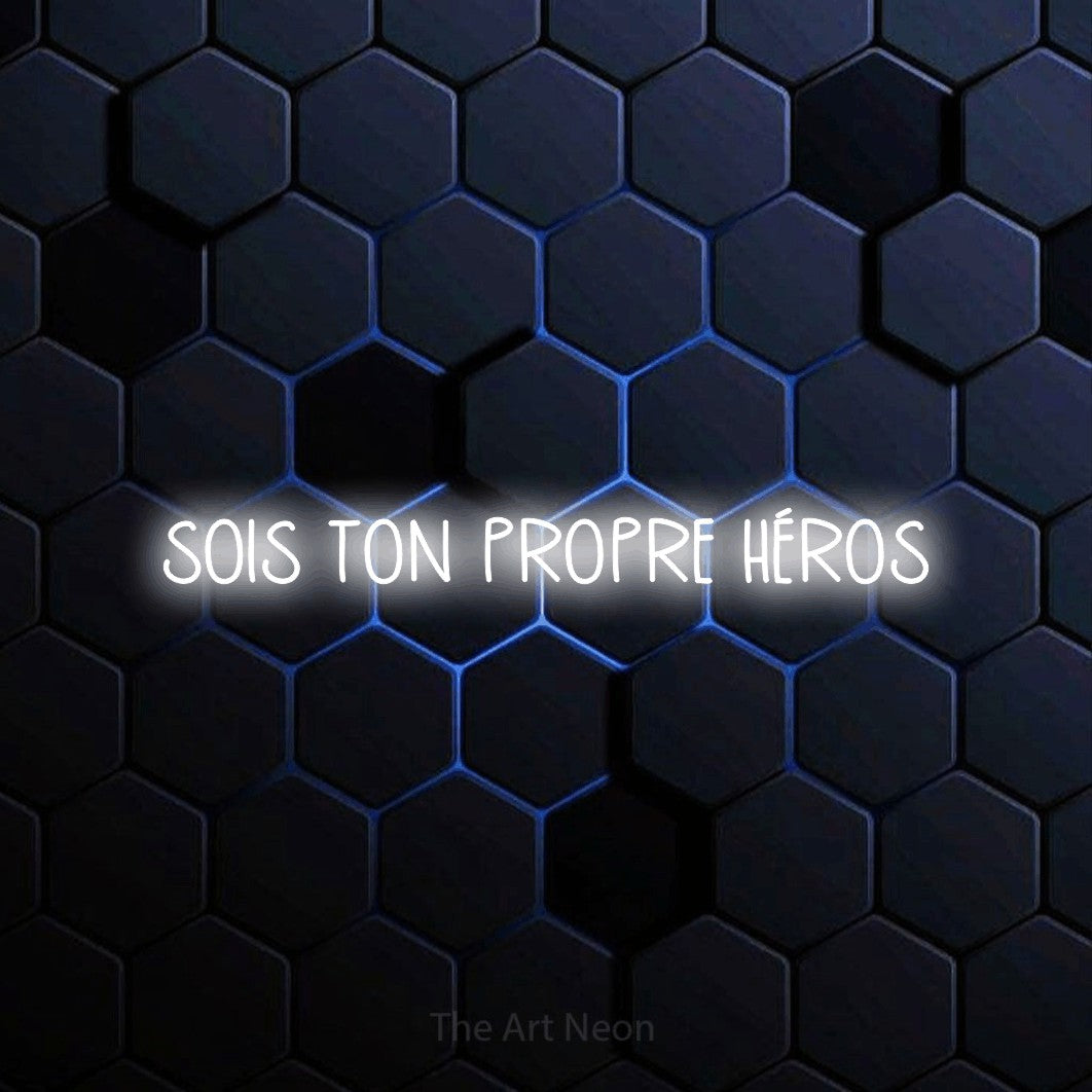 “Sois ton propre héros” LED neon sign in cool white, with narrow hand-drawn lettering, shown against a dark blue honeycomb pattern.
