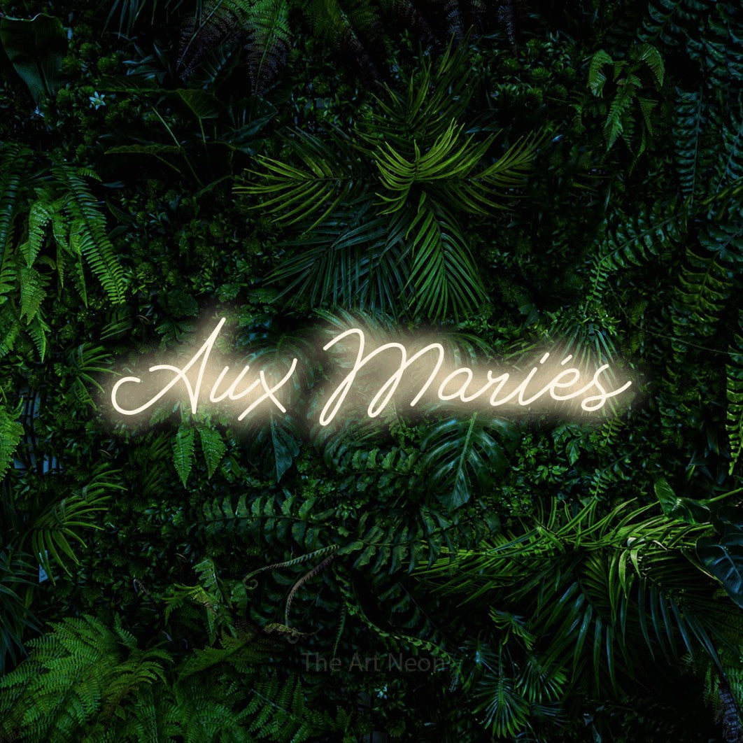 “Aux mariés” LED neon sign in warm white, with cursive lettering, shown against dense tropical foliage.